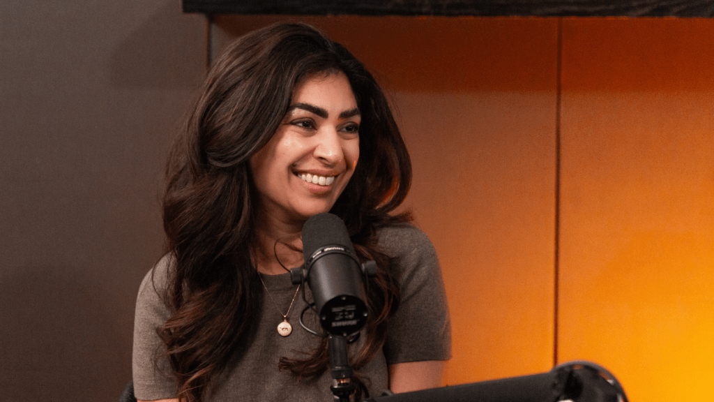 Dr. Sapna Sriram smiling while speaking into a microphone during a Table 6ix podcast recording, seated in a warmly lit studio.