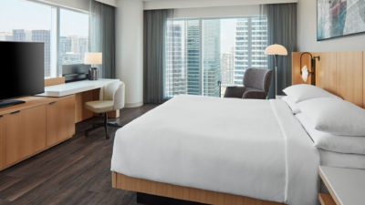 Modern hotel room in Downtown Toronto with a king bed, large floor-to-ceiling windows overlooking the city skyline, a workspace desk, and minimalist contemporary furnishings.
