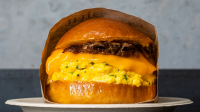 A close-up of Eggslut’s breakfast sandwich featuring soft scrambled eggs, melted cheddar cheese, and caramelized onions on a glossy brioche bun.