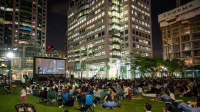 Crowds watching an outdoor movie screening at David Pecaut Square in downtown Toronto at night.