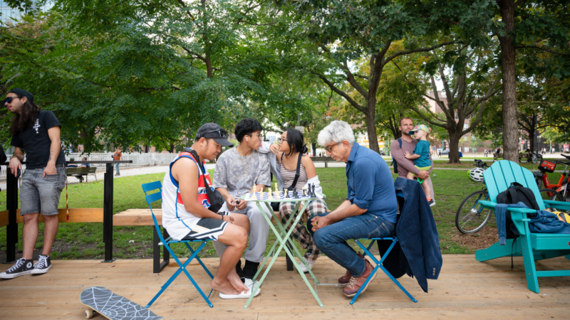 People playing chess together at an outdoor park seating area surrounded by trees in downtown Toronto.