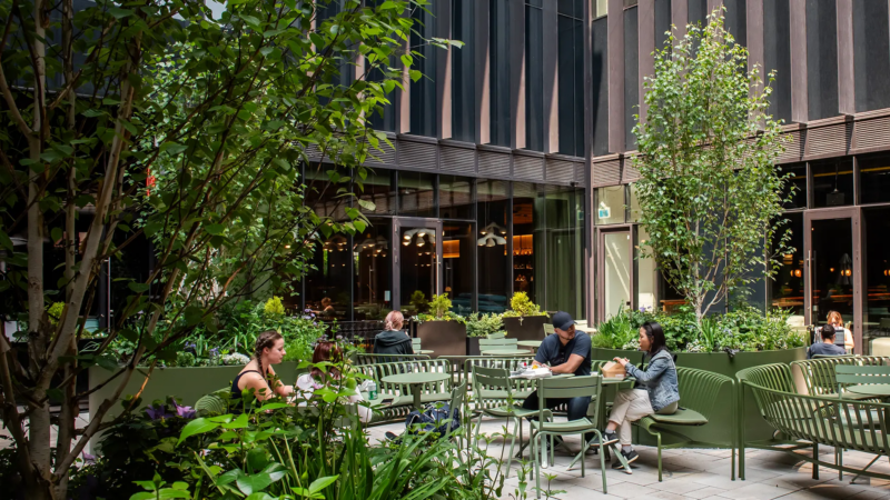 Outdoor patio seating at Waterworks Food Hall surrounded by greenery and modern buildings in downtown Toronto.